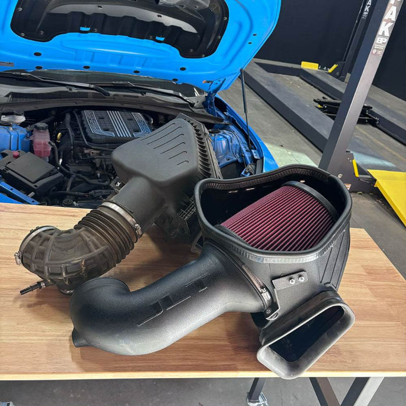 SB Filters JLT Cold Air Intake for 2017-2024 Camaro ZL1 6.2L on a wooden table with a blue car in the background