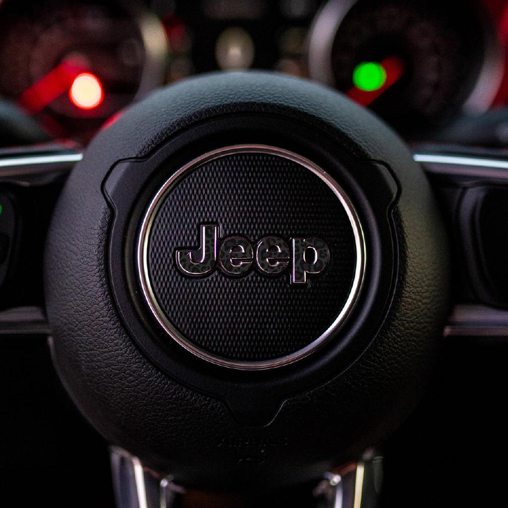 Close-up of a black leopard Jeep steering wheel logo in a car interior.